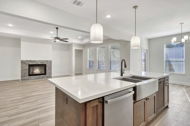 kitchen featuring dishwasher, light hardwood / wood-style floors, decorative light fixtures, and a center island with sink