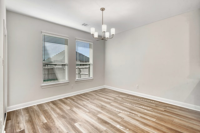 spare room with light hardwood / wood-style floors and a notable chandelier