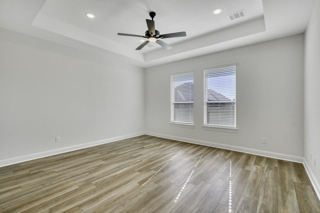 empty room featuring a tray ceiling, ceiling fan, and light hardwood / wood-style flooring