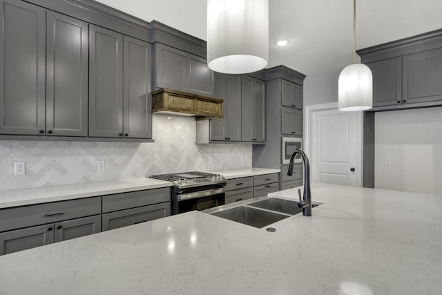 kitchen with light stone countertops, backsplash, sink, stainless steel range with gas cooktop, and hanging light fixtures