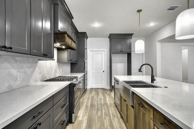 kitchen with light stone countertops, appliances with stainless steel finishes, sink, decorative light fixtures, and hardwood / wood-style floors