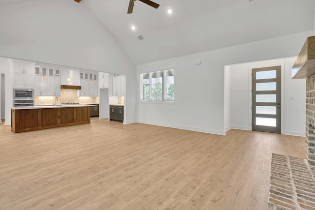 unfurnished living room with a brick fireplace, ceiling fan, light hardwood / wood-style flooring, sink, and high vaulted ceiling