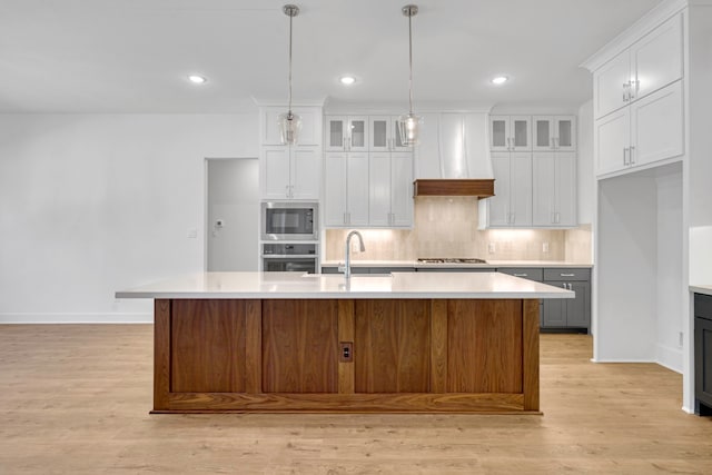 kitchen with a center island with sink, custom exhaust hood, stainless steel appliances, and white cabinets