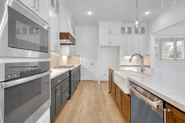 kitchen with light wood-type flooring, decorative backsplash, stainless steel appliances, white cabinets, and decorative light fixtures