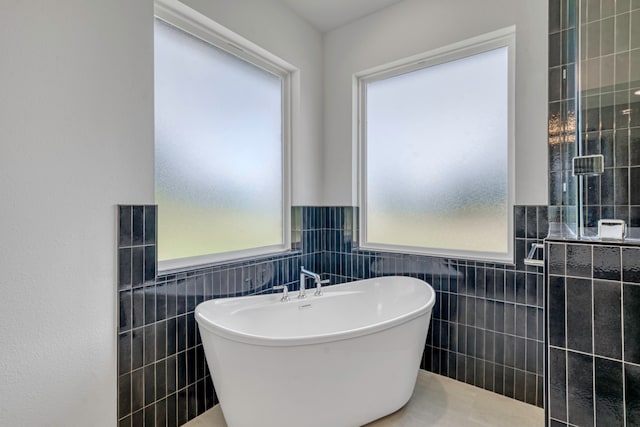 bathroom featuring a bathtub, a healthy amount of sunlight, and tile walls