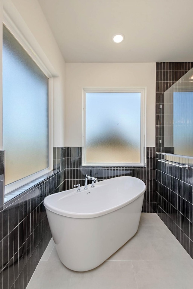 bathroom with tile patterned floors, a tub to relax in, and tile walls