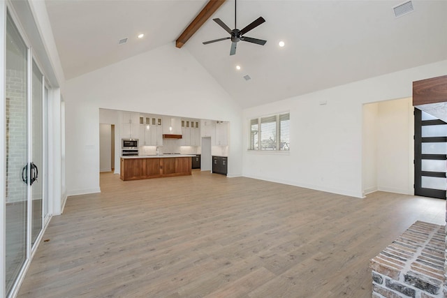 unfurnished living room with sink, high vaulted ceiling, light hardwood / wood-style flooring, ceiling fan, and beam ceiling