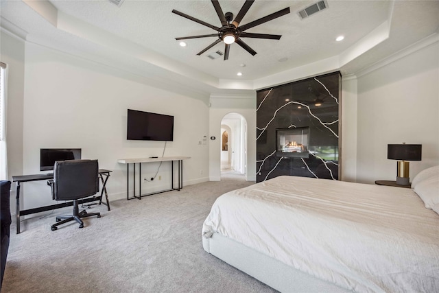 carpeted bedroom with a raised ceiling, a textured ceiling, ceiling fan, and a large fireplace