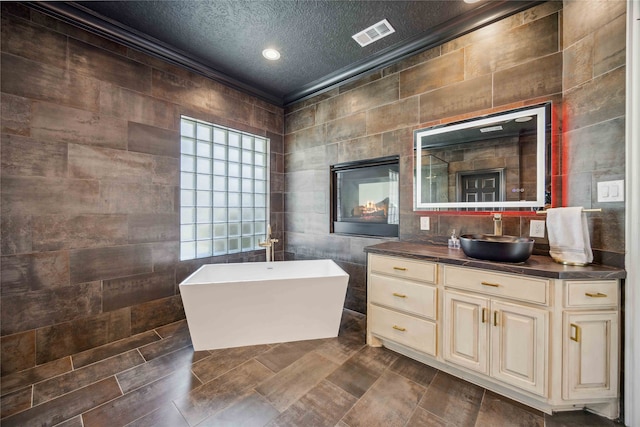 bathroom featuring a tub, ornamental molding, vanity, a textured ceiling, and tile walls