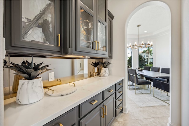 bar with gray cabinetry, light tile patterned floors, crown molding, light stone countertops, and a chandelier