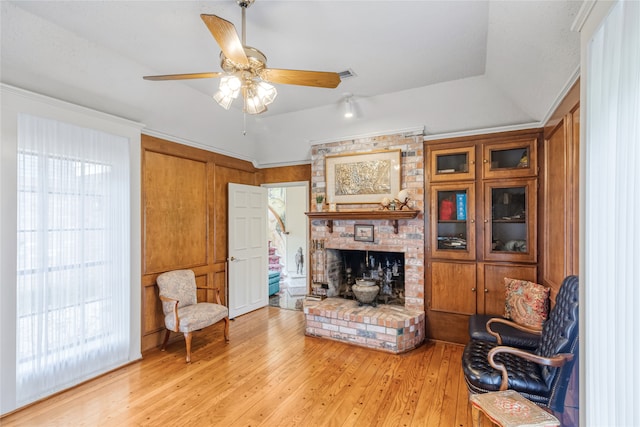 living room featuring a fireplace, light wood-type flooring, a raised ceiling, and ceiling fan