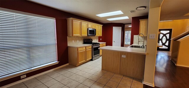 kitchen with a skylight, light hardwood / wood-style flooring, stainless steel appliances, sink, and kitchen peninsula