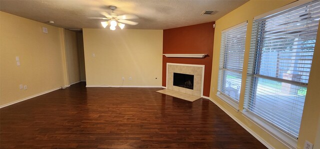 unfurnished living room featuring a textured ceiling, ceiling fan, a tiled fireplace, and dark hardwood / wood-style flooring