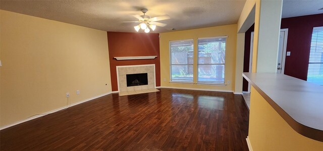 unfurnished living room with dark wood-type flooring, ceiling fan, a tiled fireplace, and a textured ceiling