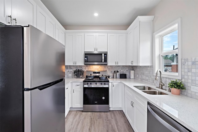 kitchen with sink, white cabinetry, stainless steel appliances, light stone counters, and decorative backsplash