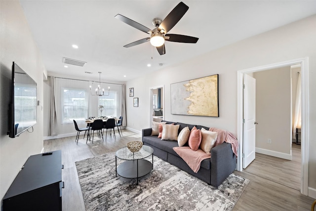 living room with ceiling fan with notable chandelier and light hardwood / wood-style flooring