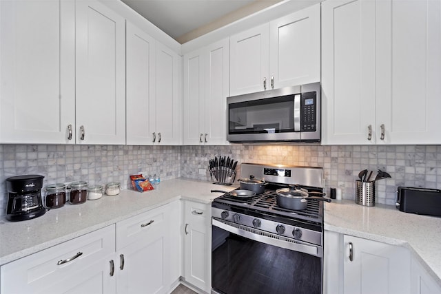 kitchen with backsplash, stainless steel appliances, white cabinets, and light stone countertops