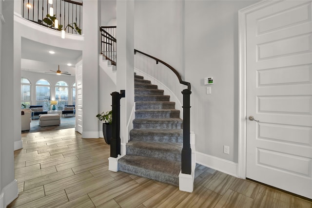 stairway featuring a towering ceiling, ceiling fan, and hardwood / wood-style flooring