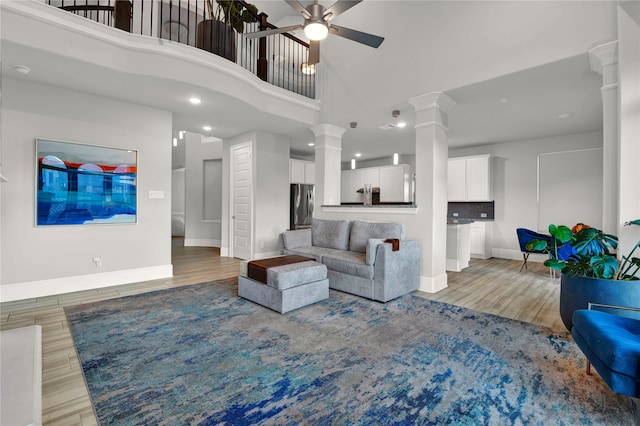 living room with ceiling fan, hardwood / wood-style floors, a towering ceiling, and ornate columns