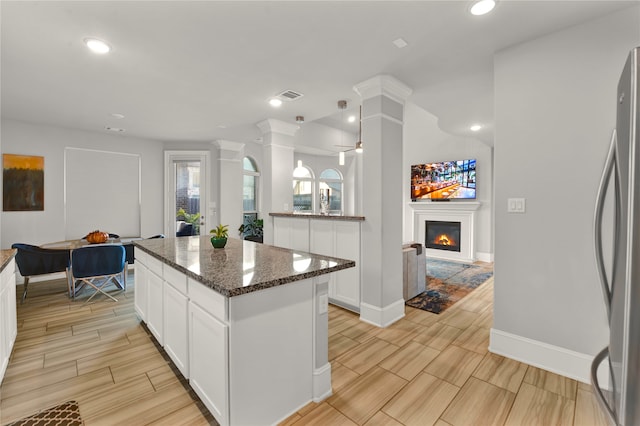 kitchen featuring stainless steel fridge, dark stone countertops, white cabinets, a kitchen island, and ceiling fan