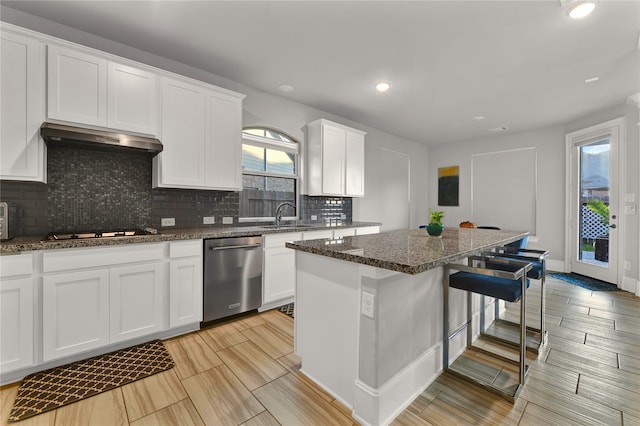 kitchen with white cabinets, a kitchen island, stainless steel dishwasher, ventilation hood, and dark stone countertops