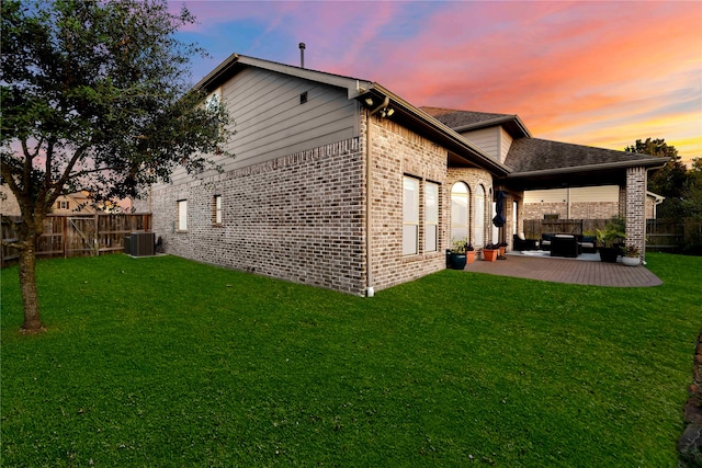 back house at dusk featuring a yard, an outdoor living space, central air condition unit, and a patio area