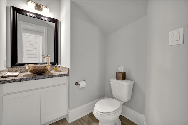 bathroom with wood-type flooring, lofted ceiling, vanity, and toilet