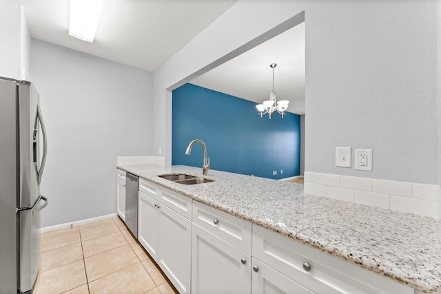 kitchen featuring light stone countertops, a chandelier, stainless steel appliances, white cabinets, and a sink