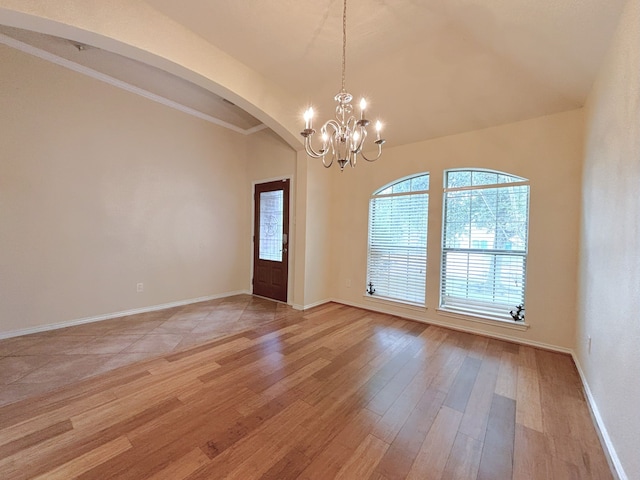 empty room with ornamental molding, vaulted ceiling, light hardwood / wood-style flooring, and a notable chandelier