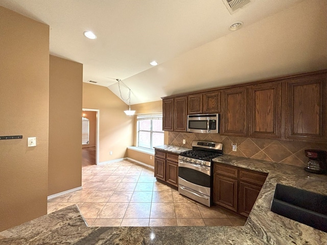 kitchen featuring dark stone countertops, pendant lighting, backsplash, appliances with stainless steel finishes, and lofted ceiling