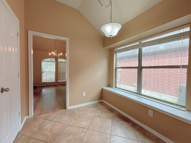 empty room featuring lofted ceiling, light wood-type flooring, and a chandelier