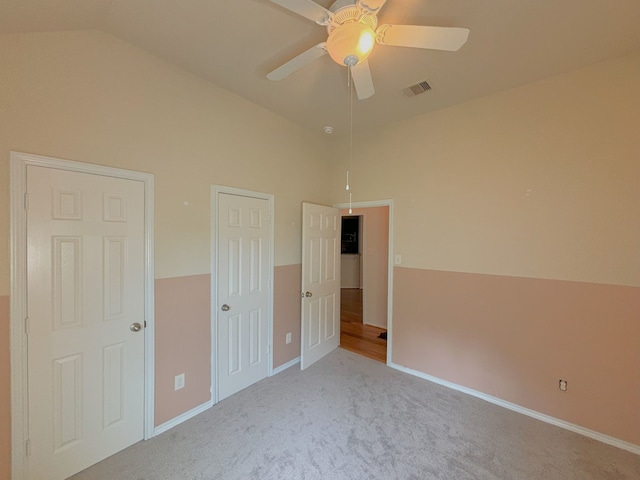 unfurnished bedroom featuring ceiling fan, carpet floors, multiple closets, and vaulted ceiling