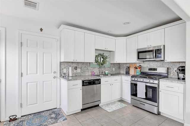 kitchen with light stone countertops, appliances with stainless steel finishes, sink, light tile patterned floors, and white cabinetry