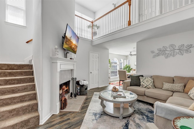 living room featuring a tile fireplace, ceiling fan, wood-type flooring, and a high ceiling