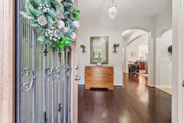 foyer entrance with dark wood finished floors, baseboards, and arched walkways