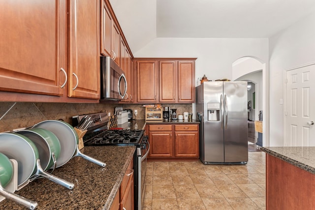 kitchen with decorative backsplash, arched walkways, brown cabinets, and stainless steel appliances