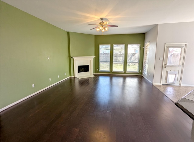 unfurnished living room with baseboards, a fireplace with flush hearth, wood finished floors, and a ceiling fan