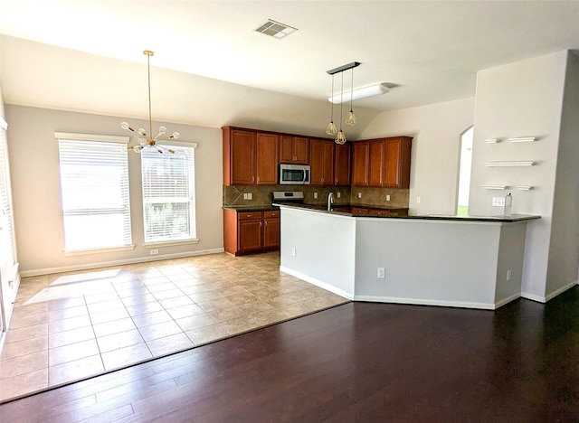 kitchen with dark countertops, visible vents, backsplash, brown cabinets, and appliances with stainless steel finishes