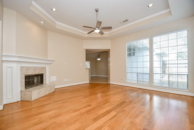 unfurnished living room featuring crown molding, a tiled fireplace, a raised ceiling, and light hardwood / wood-style floors