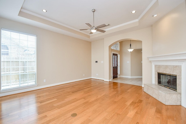 unfurnished living room featuring a fireplace, a tray ceiling, light hardwood / wood-style flooring, and ornamental molding