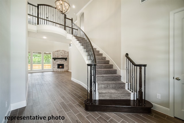 staircase featuring a high ceiling, hardwood / wood-style flooring, an inviting chandelier, and a brick fireplace