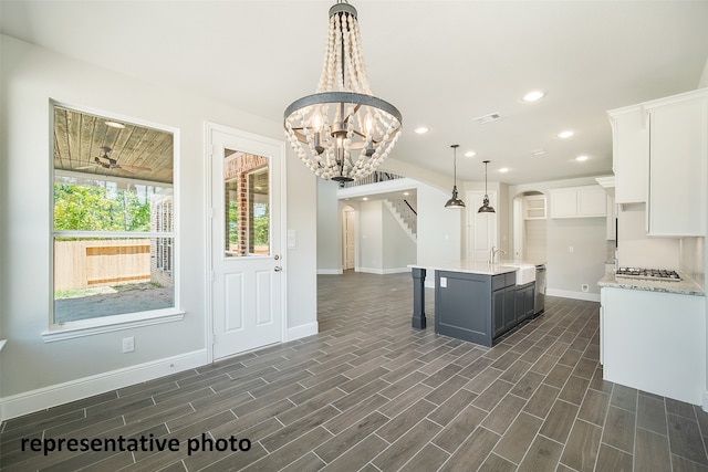 kitchen with white cabinetry, a chandelier, decorative light fixtures, an island with sink, and dark wood-type flooring