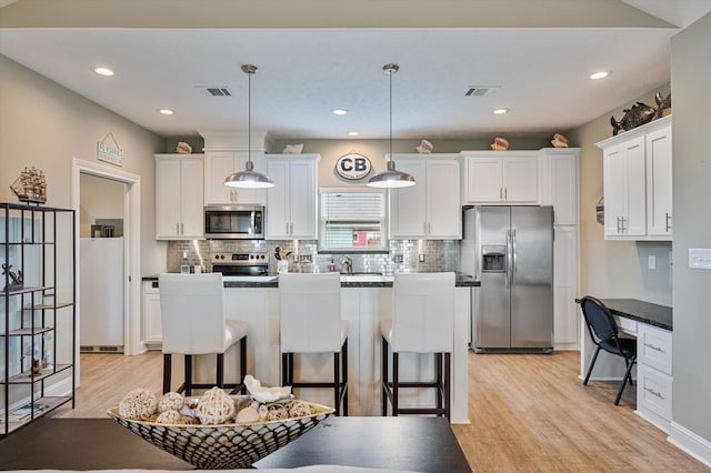 kitchen with light wood-type flooring, appliances with stainless steel finishes, white cabinetry, and a breakfast bar