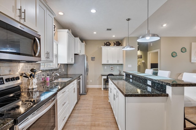 kitchen featuring a kitchen breakfast bar, stainless steel appliances, sink, white cabinetry, and light wood-type flooring