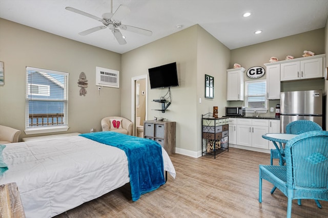 bedroom featuring stainless steel refrigerator, sink, an AC wall unit, ceiling fan, and light wood-type flooring