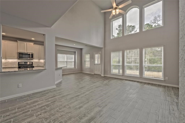 unfurnished living room with light hardwood / wood-style floors, high vaulted ceiling, plenty of natural light, and ceiling fan