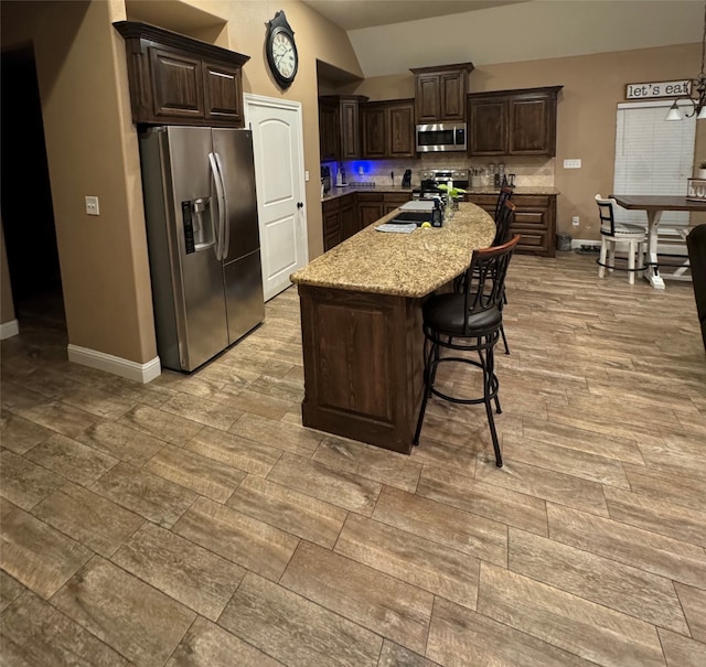 kitchen with lofted ceiling, stainless steel appliances, dark brown cabinetry, and a kitchen island with sink