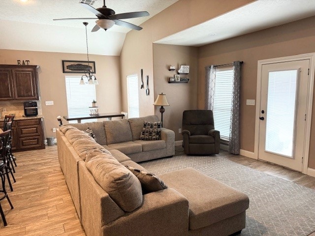 living room featuring ceiling fan with notable chandelier, lofted ceiling, and light hardwood / wood-style floors