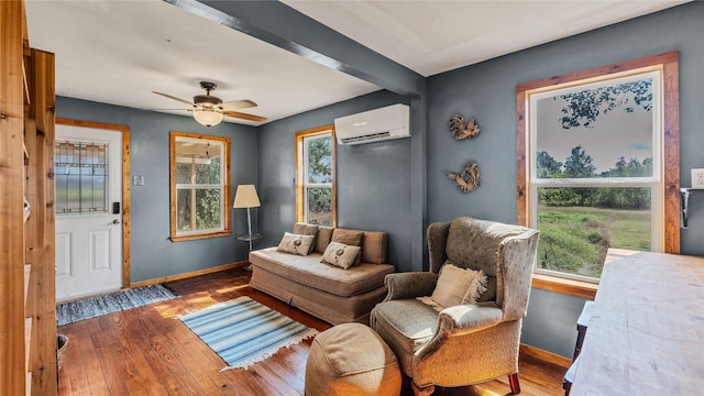 living area with an AC wall unit, baseboards, wood-type flooring, and a ceiling fan