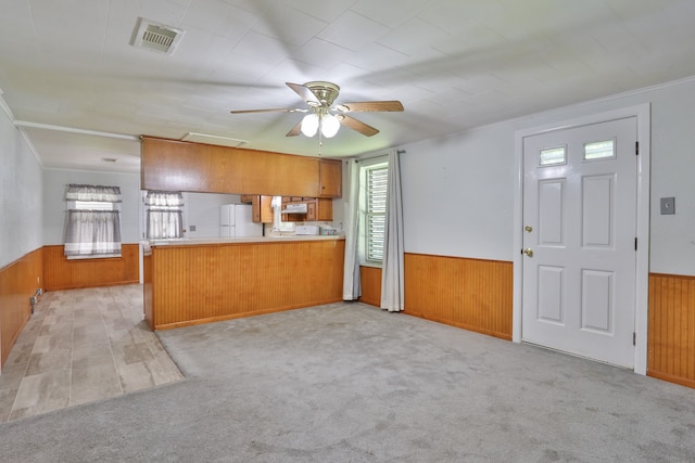 kitchen featuring light carpet, kitchen peninsula, ornamental molding, ceiling fan, and wooden walls